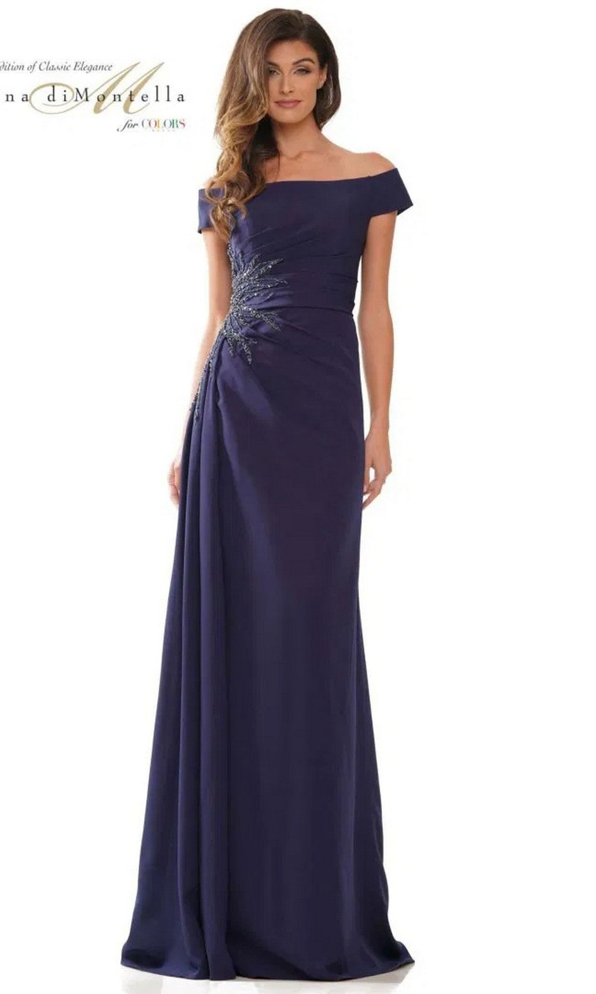 A woman stands against a white background wearing a navy Long Formal Dress (Rina Di Montella RD2806) with off-the-shoulder crepe fabric and beaded side embellishments.